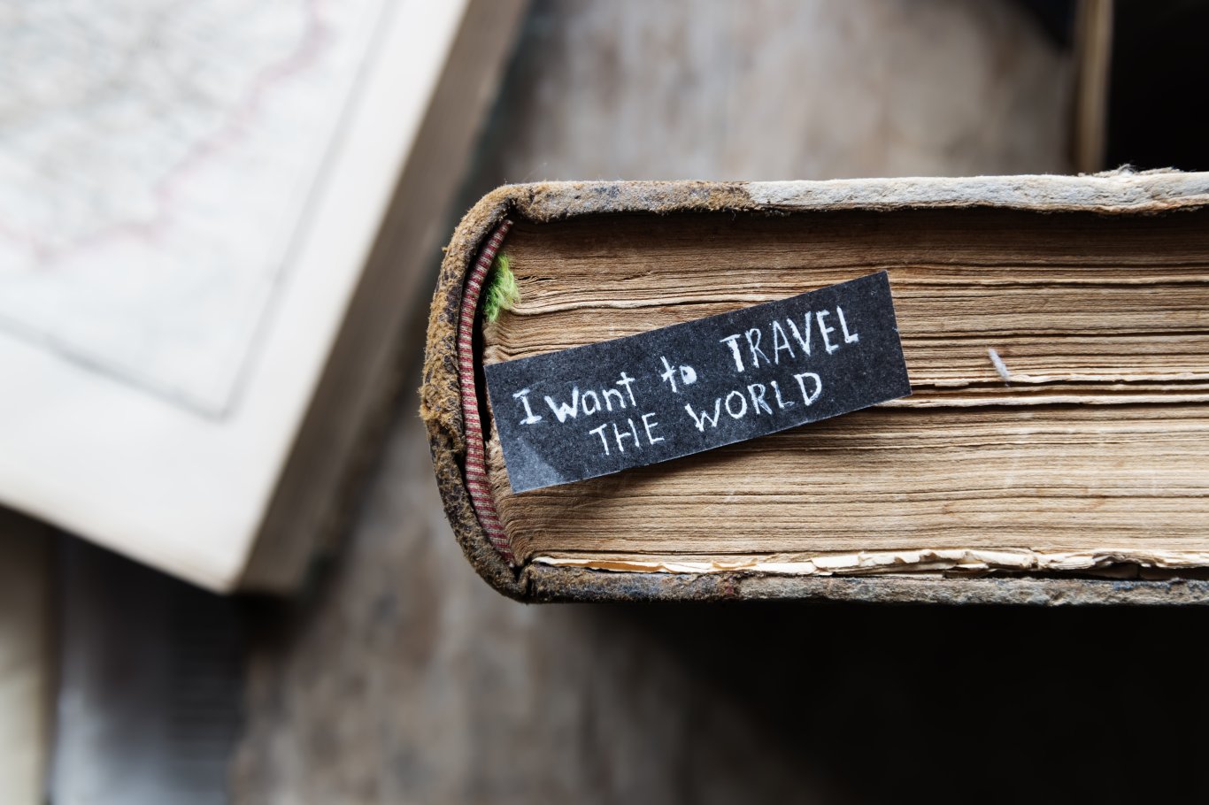 A small piece of paper with a quote that reads 'I want to travel the world' laid on a thick book