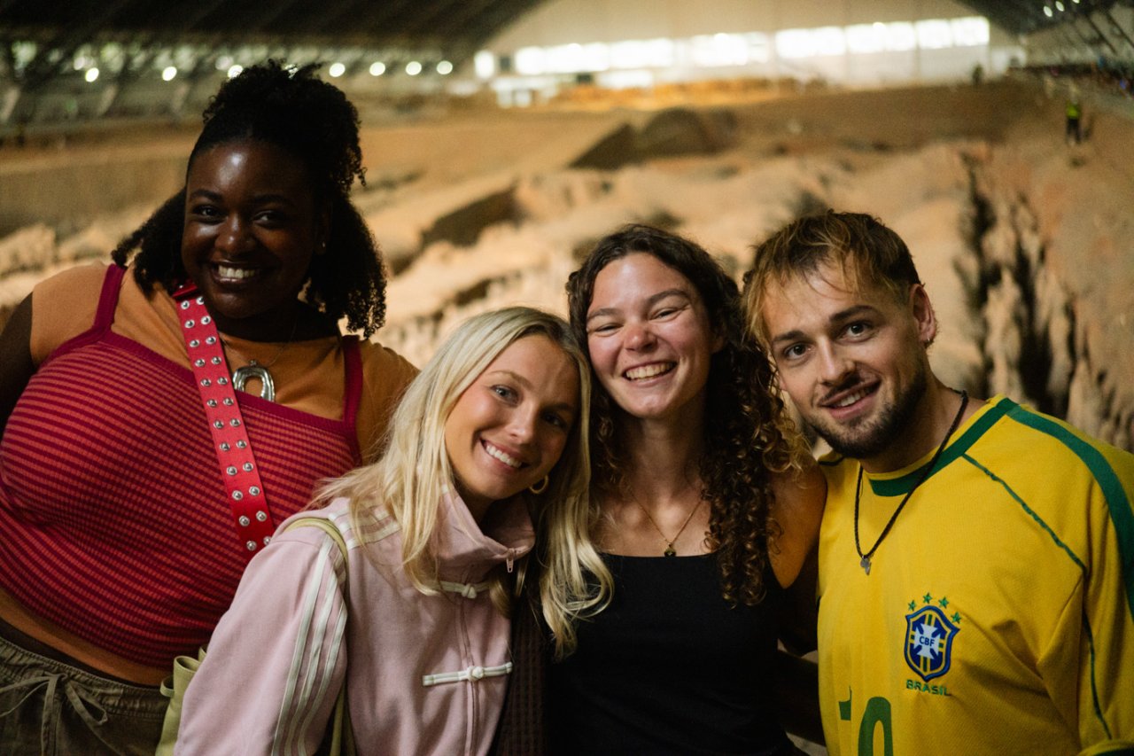 Four friends smiling inside Pit 1 of the Terracotta Army with rows of warriors behind them