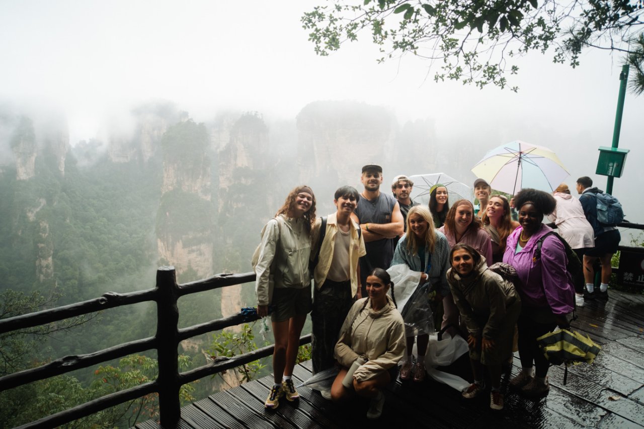 Travellers in rain jackets at a viewpoint overlooking misty sandstone pillars in Zhangjiajie National Forest Park