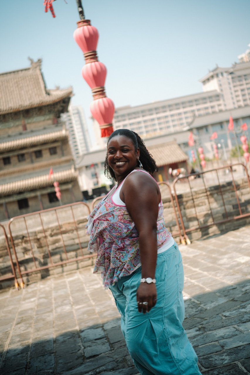 Smiling traveller on an ancient Chinese city wall with pink lanterns and a historic tower behind her