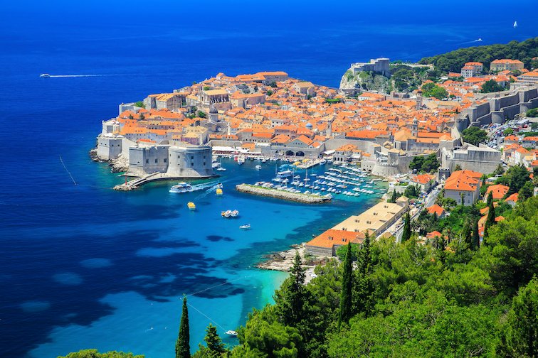 An aerial view of Dubrovnik, Croatia's scenic terracotta town, bright and deep blue ocean and greenery.