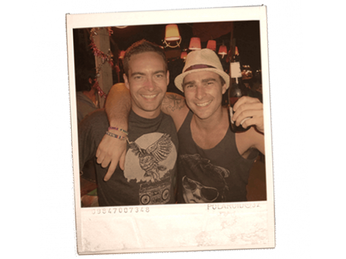 Two men smiling with arms around each other one holding a beer