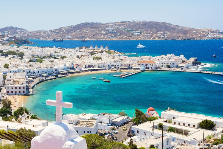 A view of the gorgeous coast in Mykonos with the bright blue water, white villas and hills in the background