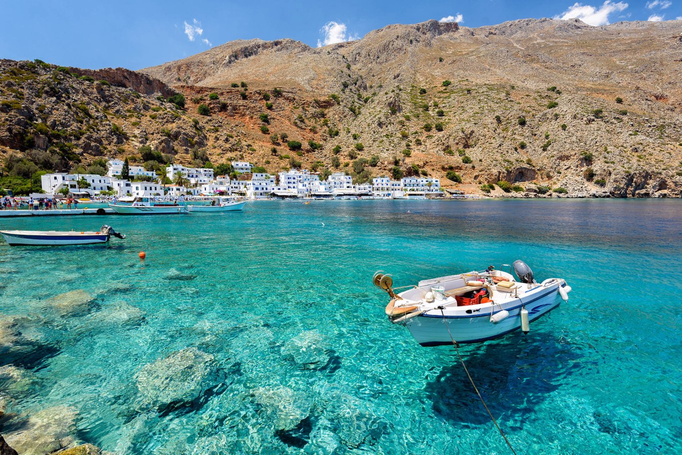 A scenic view of a small boat on the crystal clear blue water and landscapes of the Greek island in the background.
