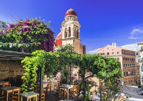 A scenic photo of Corfu town in Greece, with blue skies and a lush balcony surrounded by greenery