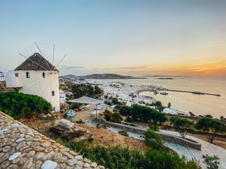 A stunning view of the harbour, town and surrounding mountains from the windmills in Mykonos, Greece at sunset 