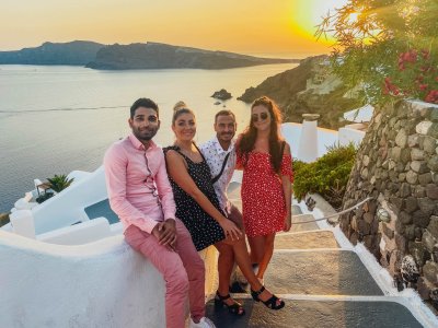A group of four on steps in front of the beautiful sunset and view of the sea & mountains in Oia, Santorini, Greece
