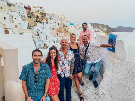 A group of six in Greece standing by Santorini's famous white houses with a view of the mountains in the background at sunset in Oia