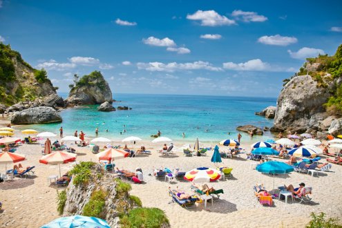 Tourists enjoying the white sandy beach and clear blue ocean in Syvota, Corfu, Greece