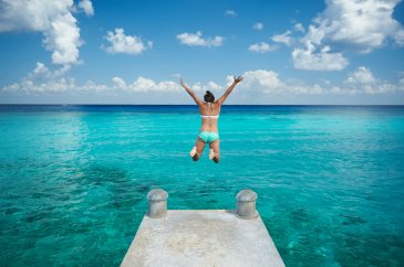 A girl jumping into the clear blue ocean 