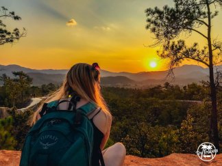 Girl sat on rock with backpack looking out to sunset 