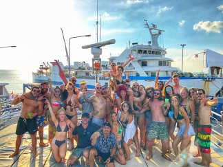large group photo with hands in the air in front of boat