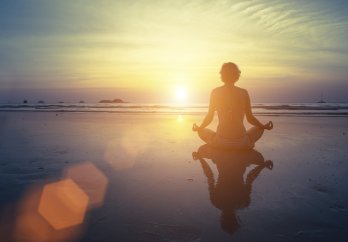 A person meditating at the beach during sunset 