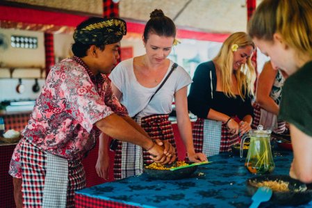Balinese man teaching girl in cooking class wearing red aprons and blue table 