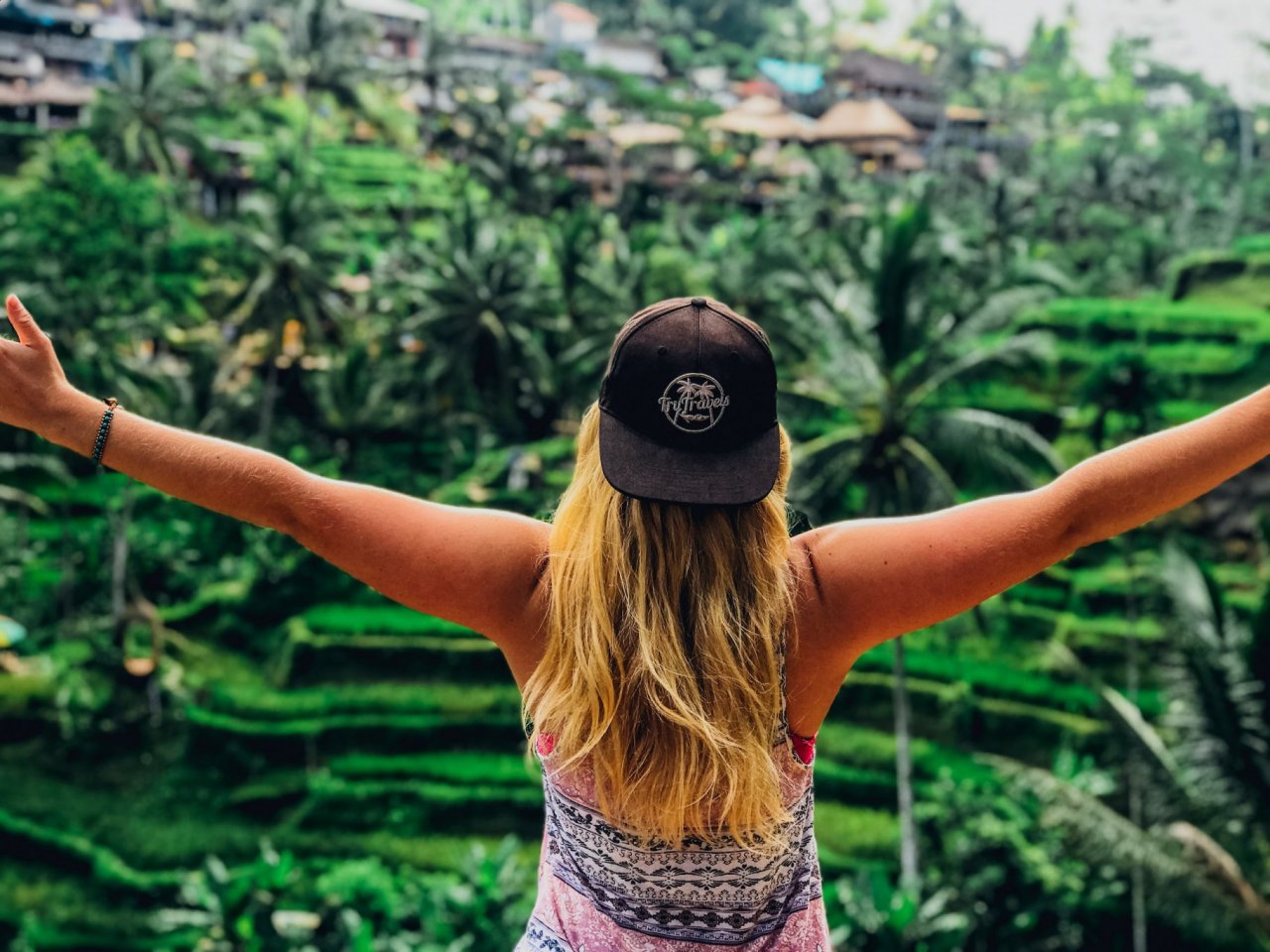A girl posing with her arms out admiring the view of the emerald green rice terraces in Ubud, Bali, Indonesia