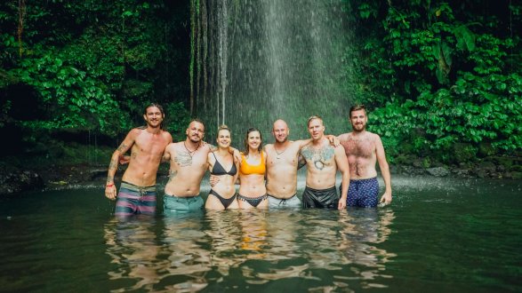 group of travellers stood in water in front of waterfall