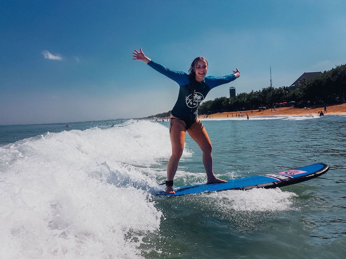 girl on surf board riding wave with arms open 
