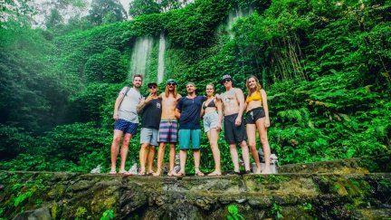 Group of travellers stood in front of waterfalls surrounded by green trees