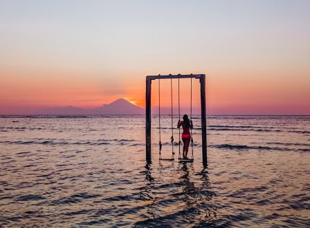 A girl on the famous swing in the sea watching the gorgeous pink sunset in Gili Trawangan Indonesia 