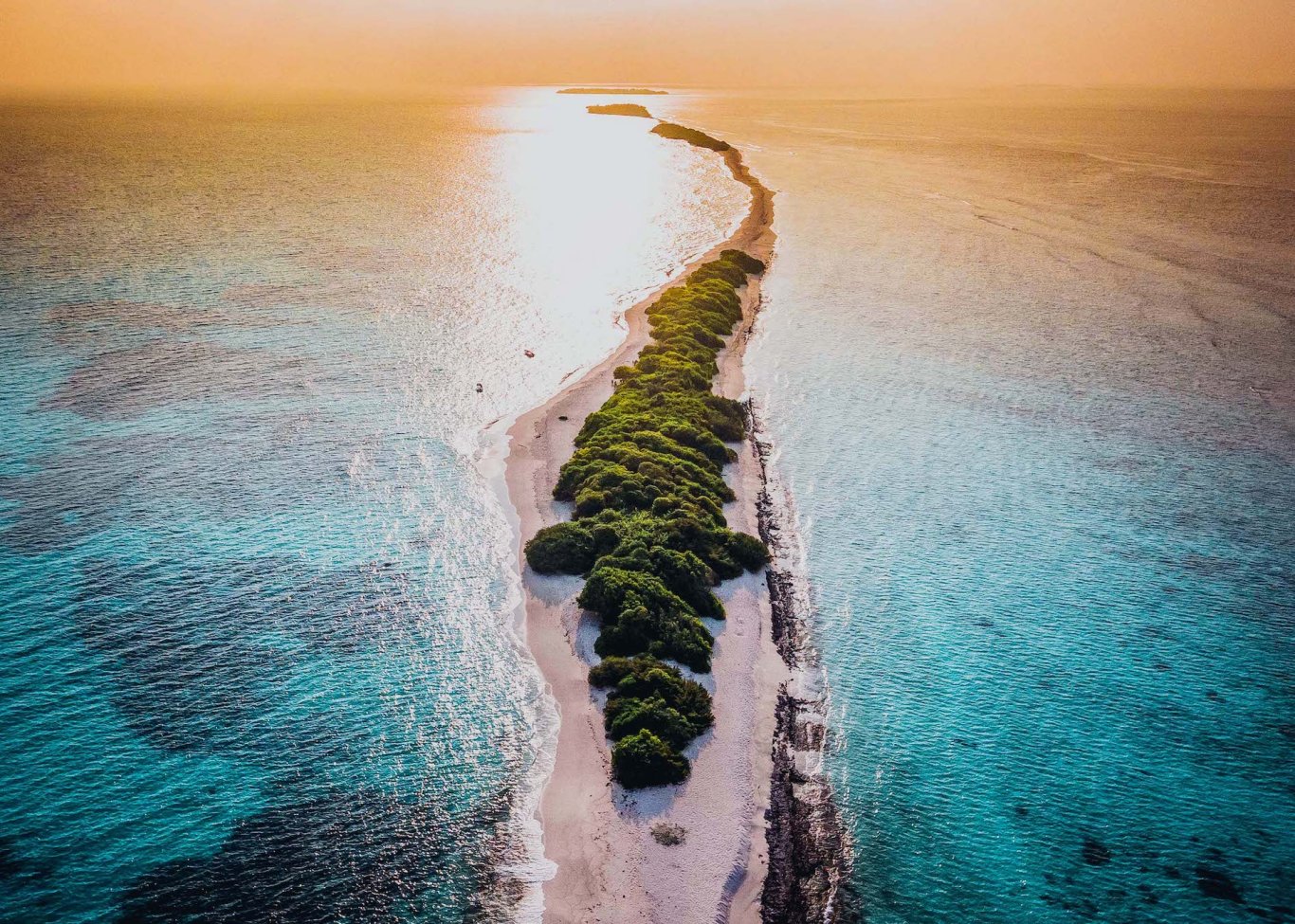 A long sandbank surrounded by bright blue water at sunset in the Maldives 