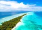 A picturesque photo of a long stretch of a sandbank surrounded by lush greenery and bright blue turquoise water with coral reefs in view 