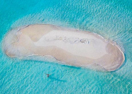 An aerial shot of a circular sand bank in the middle of the bright blue ocean in the Maldives 