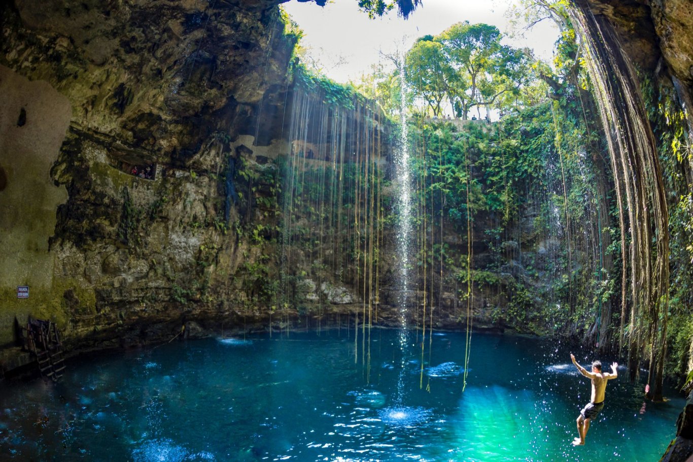 Mexican Cenote - blue water surrounded by limestone rock with man mid air jumping in the water