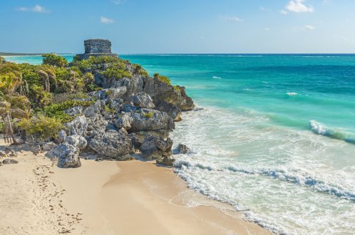 A scenic shot of the beach ruins in Tulum, Mexico showing the stunning bright blue ocean and golden sandy beach