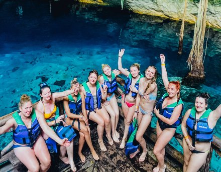 A group of individuals pose in front of the clear blue waters if Cenote Ik Kil.