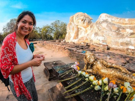 Girl standing in front of some flower offerings laid down next to a giant reclining buddha in ayutthaya, Thailand