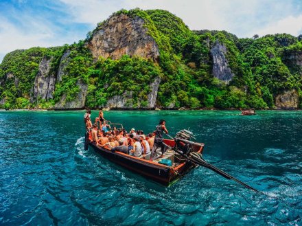 Group of people on a small boat sailing through deep blue waters and islands covered in trees surrounding them