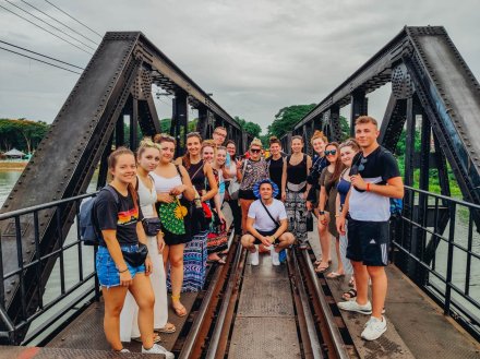 large group standing on bridge over the river kwai on a cloudy day in Thailand