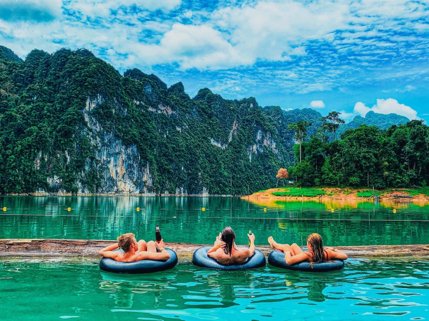 A trio admiring the view of Khao Sok national park in Thailand from doughnuts in the water