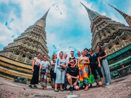 Group standing in between two temples in Bangkok with blue sky and clouds