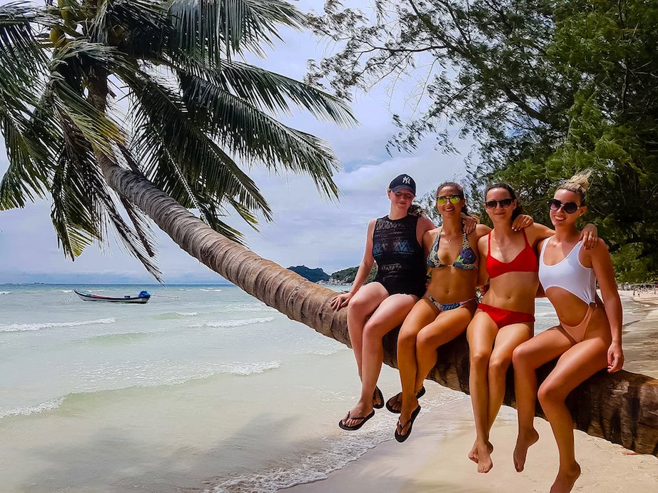 Girls sitting on palm tree on the beach, Thailand