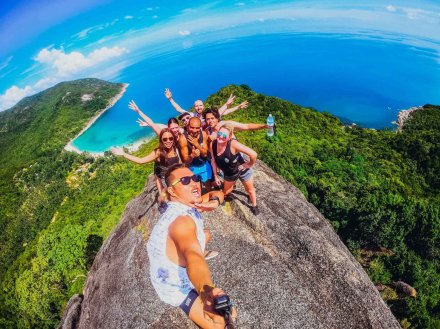 A group using a selfie stick at the top of the view point at bottle beach in Koh Phangan Thailand overlooking the lush greenery and blue sea